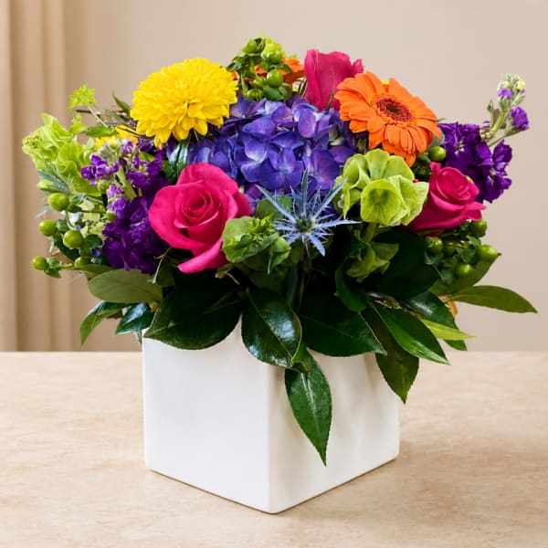 Colorful mixed flower arrangement in a white square vase