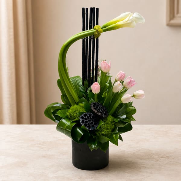 Modern floral arrangement with pink tulips and a white calla lily in a black vase