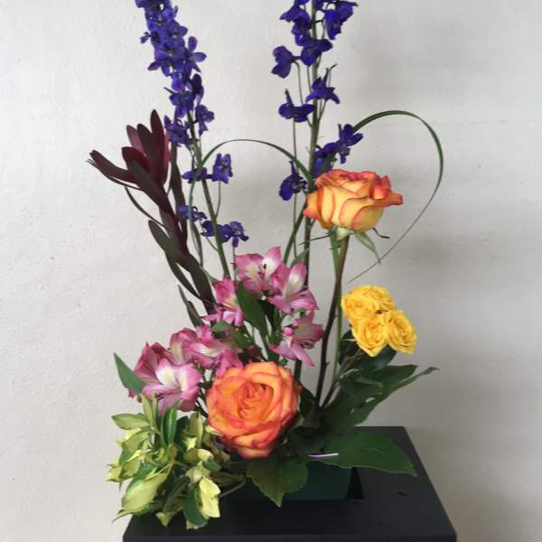 Tall floral arrangement with orange roses, pink alstroemeria, and blue delphinium