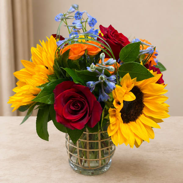 Bouquet of red roses, yellow sunflowers, and blue flowers in a glass vase