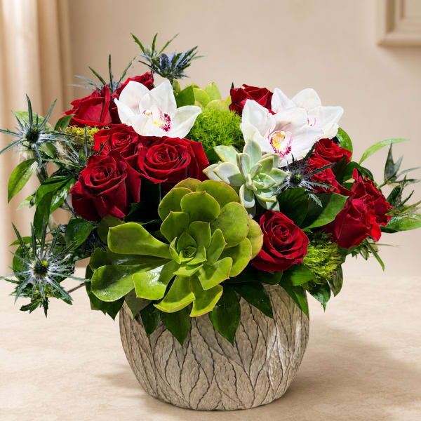 Red roses and white orchids arranged with succulents in a textured vase