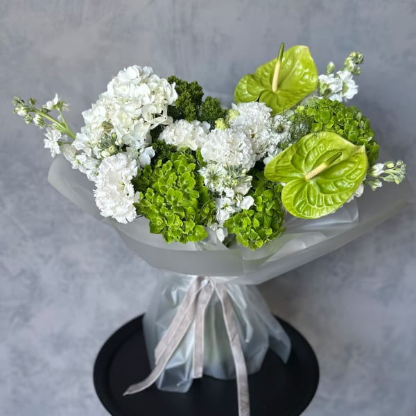 White and green bouquet with hydrangeas and anthuriums wrapped in sheer paper