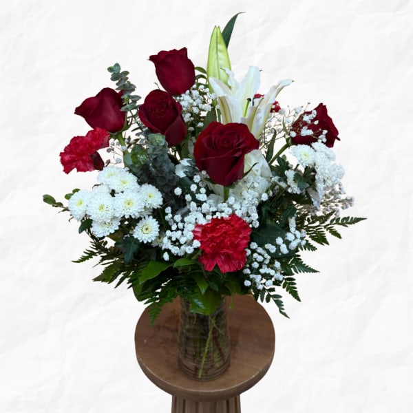 Bouquet of red roses, white lilies, and white daisies in a glass vase