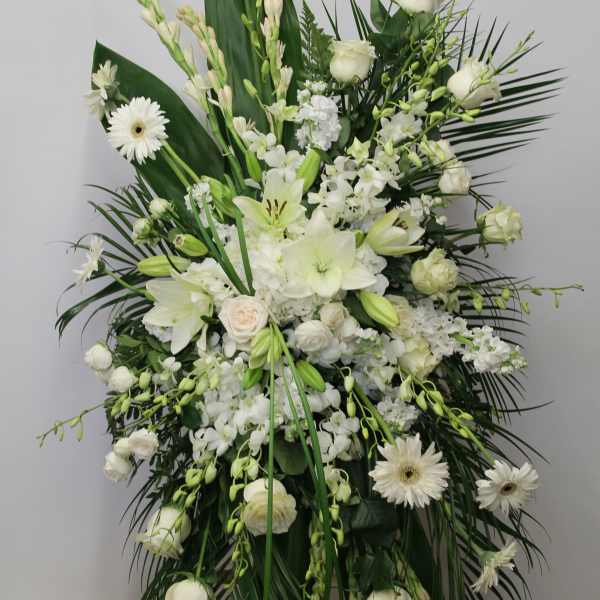 Tall white standing spray with lilies, roses, gerbera daisies, and orchids on a wooden easel