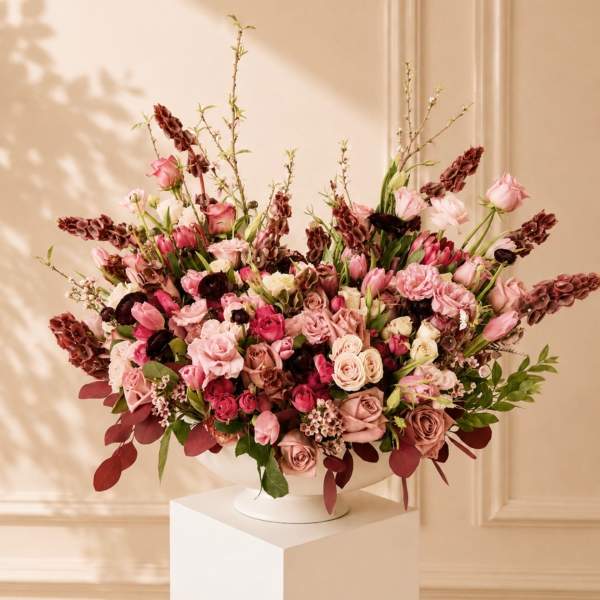 Large pink and burgundy floral arrangement in a white pedestal vase