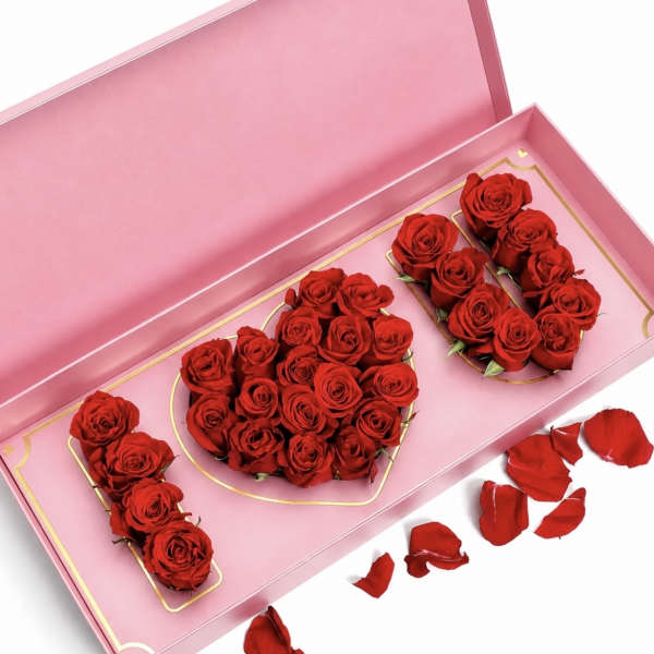 Red roses arranged in a pink gift box with scattered petals