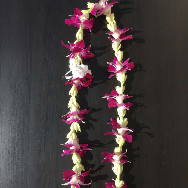 Two purple and white flower leis on a dark surface