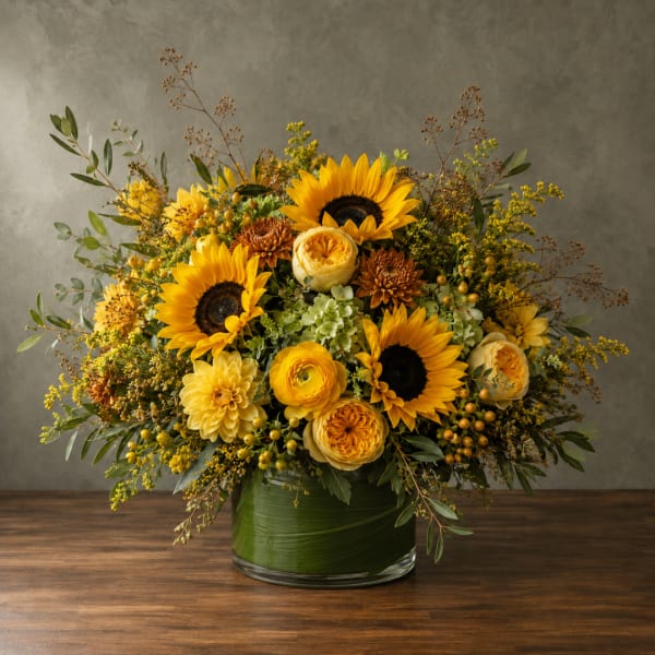Yellow sunflowers and mixed blooms arranged in a green glass vase