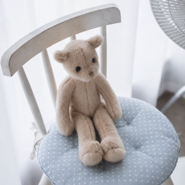 Small beige teddy bear sitting on a blue polka dot chair cushion