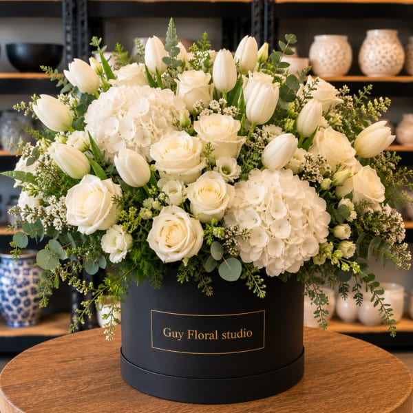 White roses and tulips arranged in a black hat box