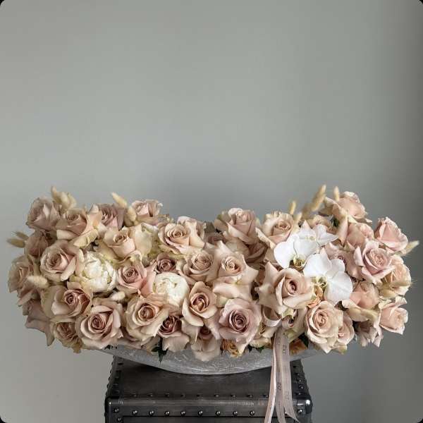 Low arrangement of blush roses and white orchids in a shallow container