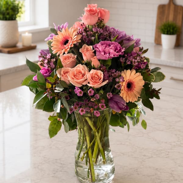 Mixed pink and purple flowers arranged in a clear glass vase