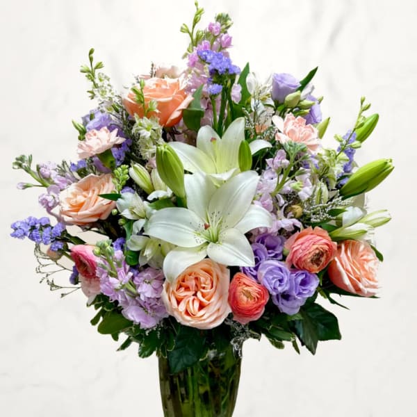 Mixed bouquet of lilies, roses, and purple flowers in a glass vase