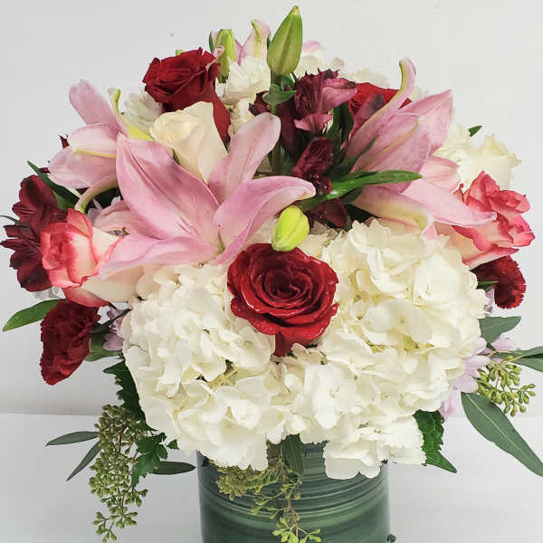 Bouquet of pink lilies, red roses, and white hydrangeas in a green vase