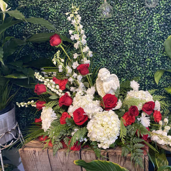 Red roses and white flowers arranged around a small angel figurine