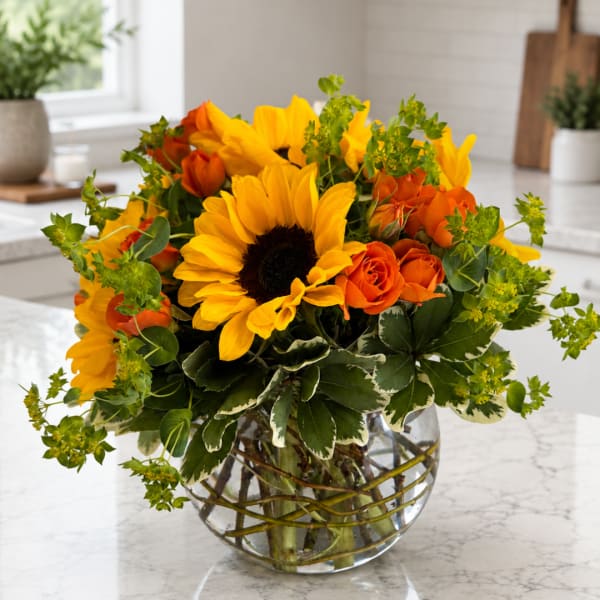 Sunflowers and orange roses arranged in a clear glass vase