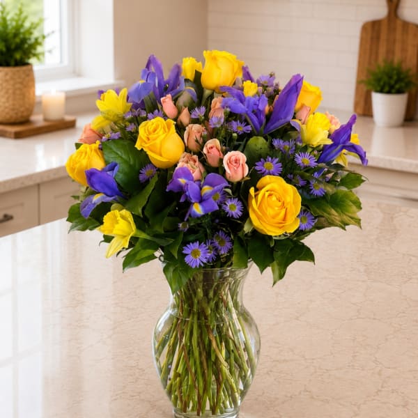 Bouquet of yellow roses, purple irises, and pink spray roses in a glass vase