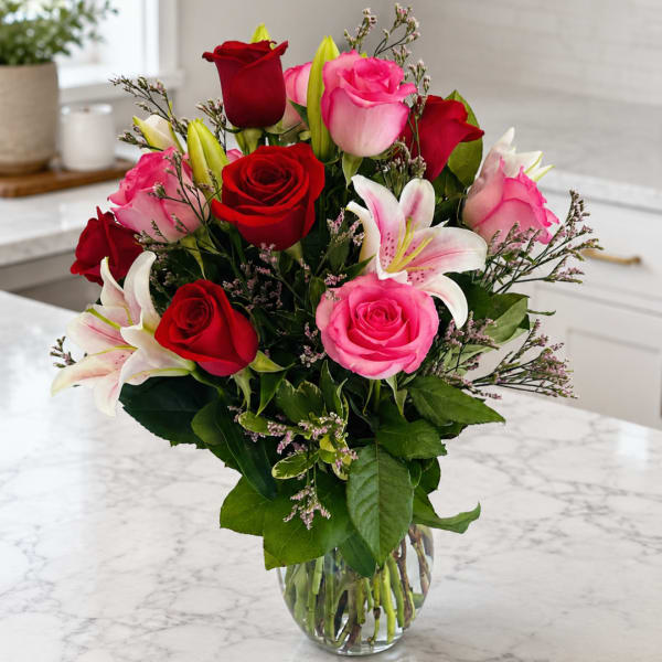 Bouquet of red and pink roses with white lilies in a clear glass vase