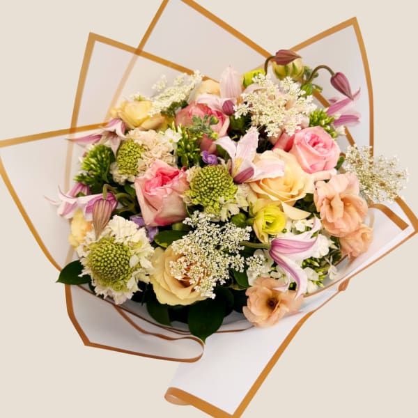 Mixed bouquet of pink, peach, and cream flowers wrapped in white paper with gold trim