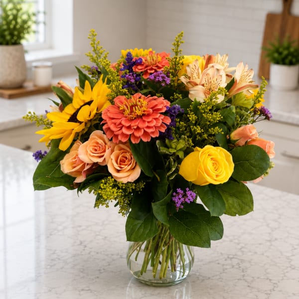 Mixed bouquet of yellow, peach, and purple flowers in a clear glass vase