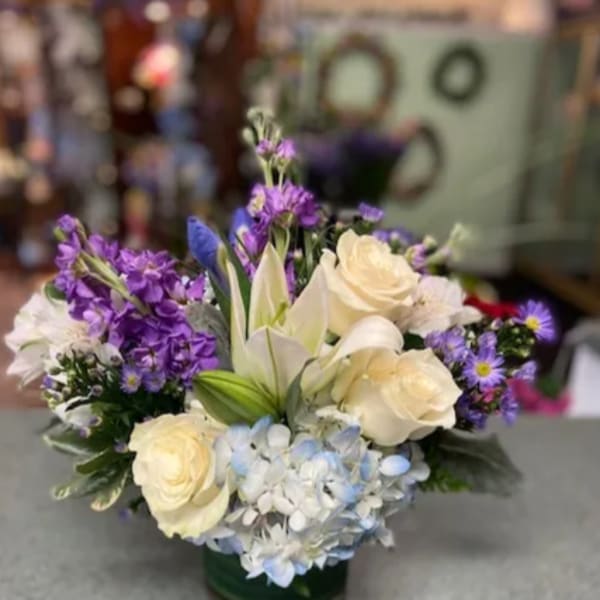 Bouquet of cream roses, lilies, and purple flowers in a glass vase