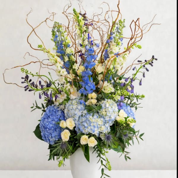 Tall blue and white floral arrangement in a white vase with curly branches
