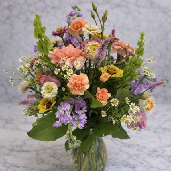 Mixed bouquet of peach, purple, white, and yellow flowers in a clear vase