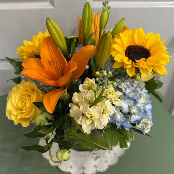 Bouquet of yellow and orange flowers with blue hydrangeas in a vase