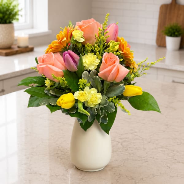 Mixed bouquet of roses, tulips, and daisies in a white vase