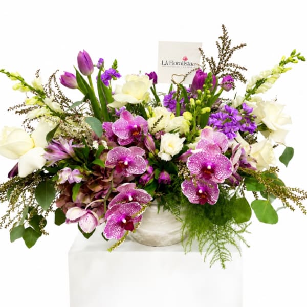 Mixed bouquet with purple orchids, white calla lilies, and tulips in a white vase