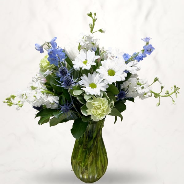 White daisies and blue flowers arranged in a green glass vase