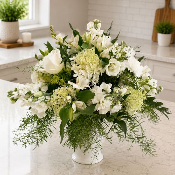 White floral arrangement in a white vase with trailing greenery