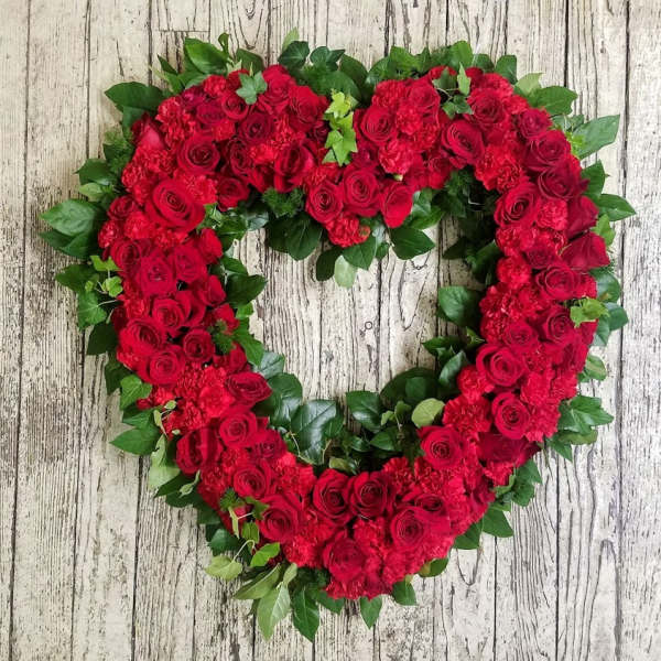 Heart-shaped wreath of red roses and greenery on a wood background