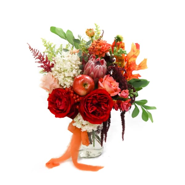 Mixed bouquet of red roses, white hydrangea, and autumn accents in a glass vase