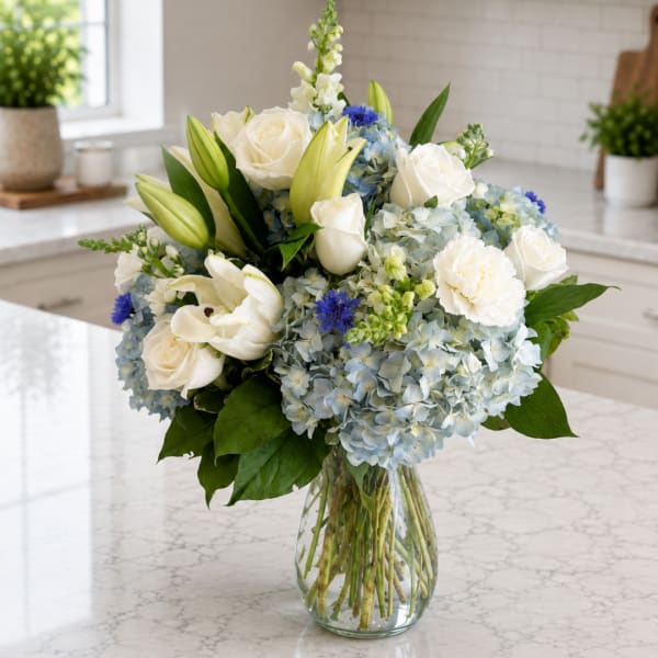 White roses, lilies, and blue hydrangeas in a clear glass vase