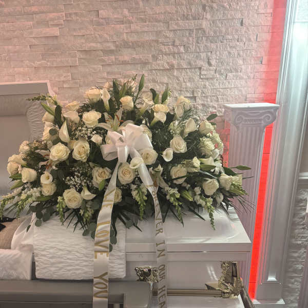 White rose funeral casket spray with lilies and ribbon on a casket
