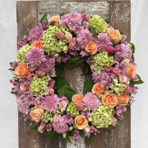 Floral wreath with pink and peach blooms on a rustic wooden board
