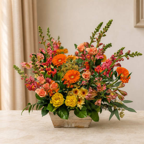 Mixed bouquet of orange, pink, and yellow flowers in a wooden container