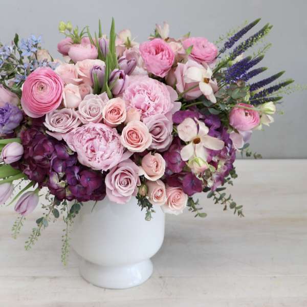 Low pink and purple flower arrangement with roses and peonies in a white ceramic vase.