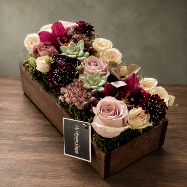 Rectangular floral arrangement with roses, orchids, and succulents in a wooden box