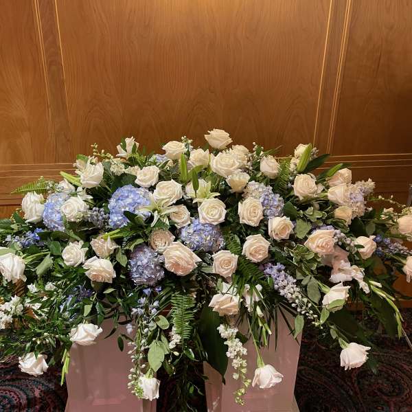 Large funeral spray of white roses and blue hydrangeas in a container