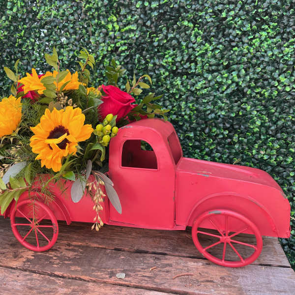 Pink toy truck filled with sunflowers and red roses