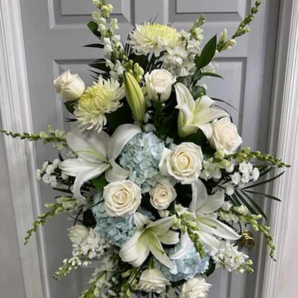 White floral standing spray with lilies, roses, and blue hydrangeas on an easel