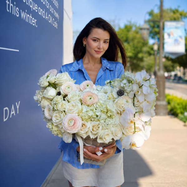 Woman holding a large heart-shaped bouquet of white and blush flowers