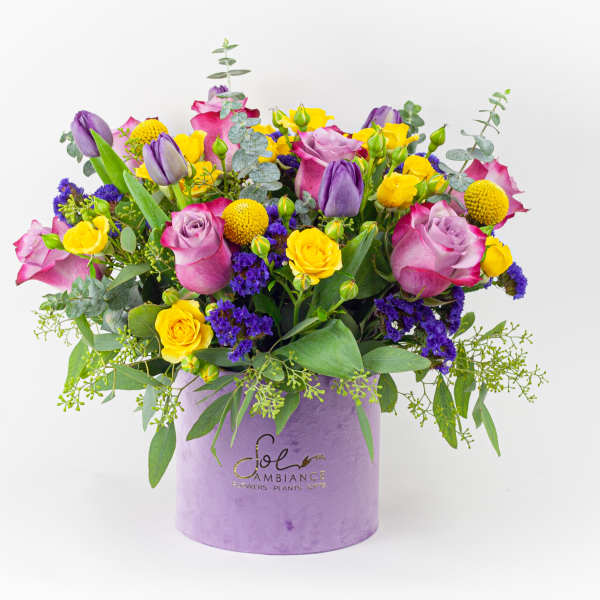 Mixed bouquet of pink, purple, and yellow flowers in a lavender box