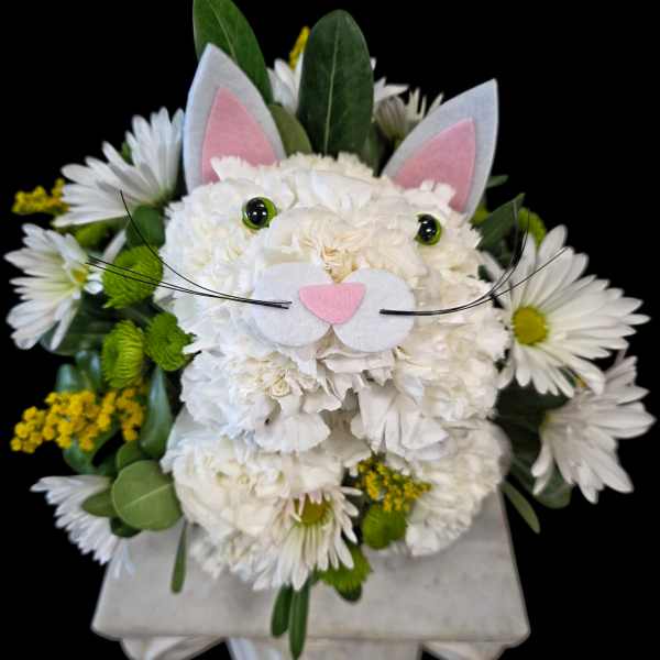 White floral arrangement styled as a cat face with pink ears and whiskers