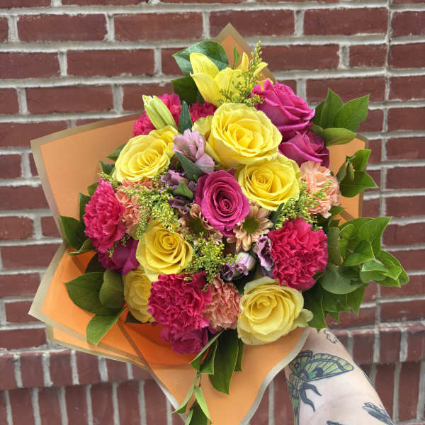 Handheld bouquet of yellow and pink roses with carnations in orange wrap