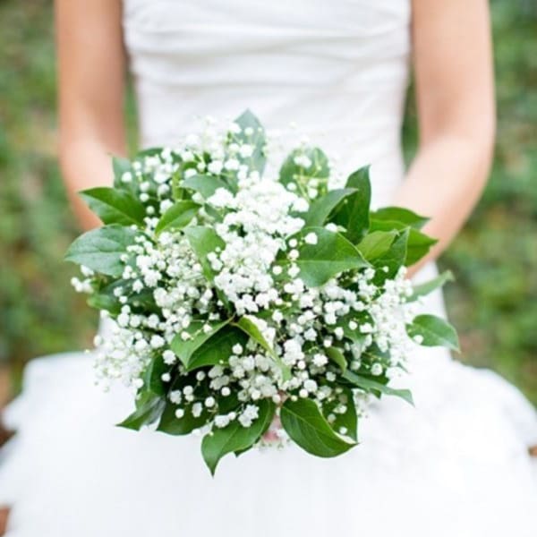 Bride holding a white bouquet with baby's breath and green leaves