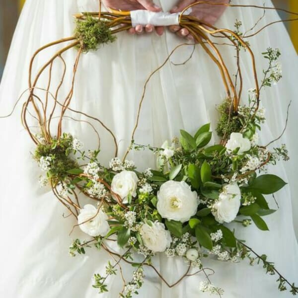 White floral wreath with green foliage and twisting branches held by a person