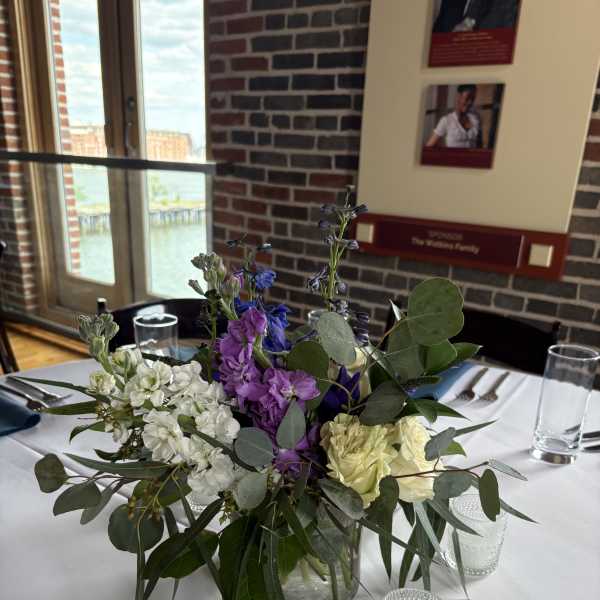 Mixed purple, white, and pale yellow flowers in a clear glass vase on a table